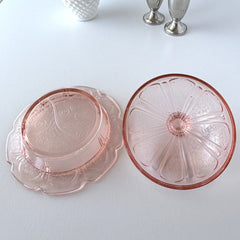 Vintage Jeannette Cherry Blossom pink Depression glass butter dish with embossed floral pattern, scalloped edges, and domed lid, shown in natural light on a white tabletop.
