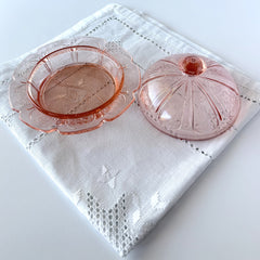 Vintage Jeannette Cherry Blossom pink Depression glass butter dish with embossed floral pattern, scalloped edges, and domed lid, shown in natural light on a white tabletop.