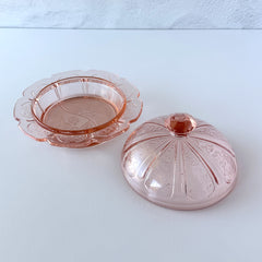 Vintage Jeannette Cherry Blossom pink Depression glass butter dish with embossed floral pattern, scalloped edges, and domed lid, shown in natural light on a white tabletop.