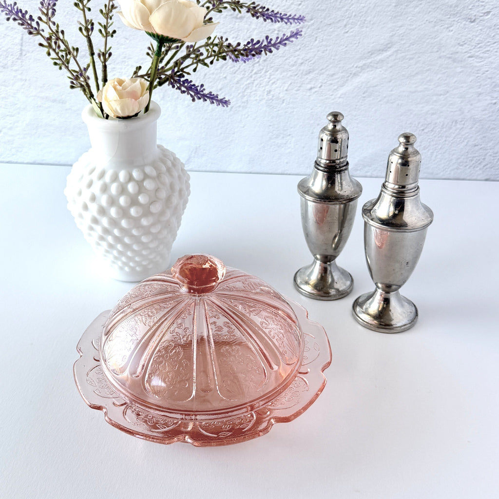Vintage Jeannette Cherry Blossom pink Depression glass butter dish with embossed floral pattern, scalloped edges, and domed lid, shown in natural light on a white tabletop.