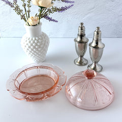 Vintage Jeannette Cherry Blossom pink Depression glass butter dish with embossed floral pattern, scalloped edges, and domed lid, shown in natural light on a white tabletop.