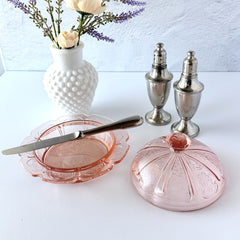 Vintage Jeannette Cherry Blossom pink Depression glass butter dish with embossed floral pattern, scalloped edges, and domed lid, shown in natural light on a white tabletop.