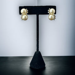 Vintage Jomaz clip-on earrings featuring two cream faux pearls accented with clear rhinestones in a silver-tone setting, signed on the back, shown in very good condition.