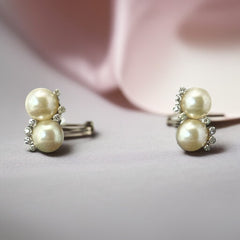 Vintage Jomaz clip-on earrings featuring two cream faux pearls accented with clear rhinestones in a silver-tone setting, signed on the back, shown in very good condition.