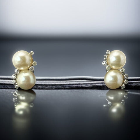 Vintage Jomaz clip-on earrings featuring two cream faux pearls accented with clear rhinestones in a silver-tone setting, signed on the back, shown in very good condition.