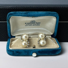Vintage Jomaz clip-on earrings featuring two cream faux pearls accented with clear rhinestones in a silver-tone setting, signed on the back, shown in very good condition.