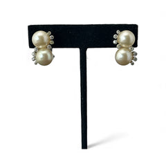 Vintage Jomaz clip-on earrings featuring two cream faux pearls accented with clear rhinestones in a silver-tone setting, signed on the back, shown in very good condition.