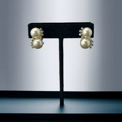 Vintage Jomaz clip-on earrings featuring two cream faux pearls accented with clear rhinestones in a silver-tone setting, signed on the back, shown in very good condition.