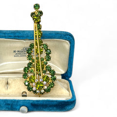 Vintage Juliana violin brooch in gold tone metal with green and peridot rhinestones, featuring layered construction and floral accents; verified design #3151 from the 1960s, shown from front and back.