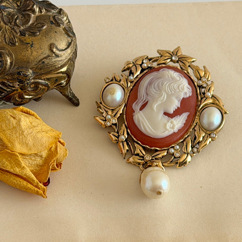 Vintage KJL for Avon gold tone cameo brooch pendant with resin cameo, faux pearls, clear rhinestones, and ornate detailing.