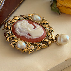 Vintage KJL for Avon gold tone cameo brooch pendant with resin cameo, faux pearls, clear rhinestones, and ornate detailing.