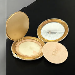 Vintage 1950s Kigu gold-tone powder compact with guilloché moiré lid, original puff, and mirror—collectible beauty accessory with timeless charm.
