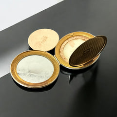 Vintage 1950s Kigu gold-tone powder compact with guilloché moiré lid, original puff, and mirror—collectible beauty accessory with timeless charm.
