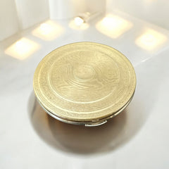 Vintage 1950s Kigu gold-tone powder compact with guilloché moiré lid, original puff, and mirror—collectible beauty accessory with timeless charm.
