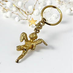 Gold-tone vintage Kirk’s Folly keychain featuring a winged cherub holding a small object, with a dangling star charm; detailed and symbolic design from the late 1980s–early 1990s.