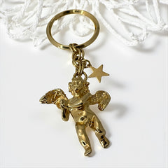 Gold-tone vintage Kirk’s Folly keychain featuring a winged cherub holding a small object, with a dangling star charm; detailed and symbolic design from the late 1980s–early 1990s.