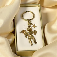 Gold-tone vintage Kirk’s Folly keychain featuring a winged cherub holding a small object, with a dangling star charm; detailed and symbolic design from the late 1980s–early 1990s.