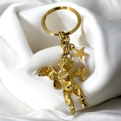 Gold-tone vintage Kirk’s Folly keychain featuring a winged cherub holding a small object, with a dangling star charm; detailed and symbolic design from the late 1980s–early 1990s.