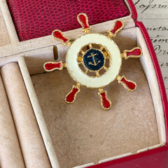 Vintage Louis Giusti gold‑tone ship‑wheel brooch with white, red, and navy enamel and anchor motif, displayed on antique paper background.