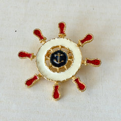 Vintage Louis Giusti gold‑tone ship‑wheel brooch with white, red, and navy enamel and anchor motif, displayed on antique paper background.