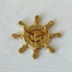 Vintage Louis Giusti gold‑tone ship‑wheel brooch with white, red, and navy enamel and anchor motif, displayed on antique paper background.
