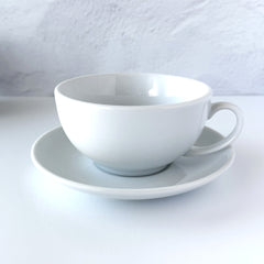 White porcelain teapot‑and‑cup set from La Route des Comptoirs with the boat‑and‑tea‑leaf logo on each piece