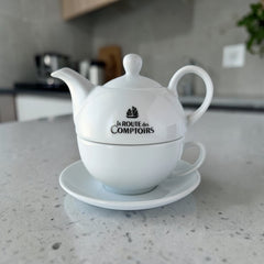 White porcelain teapot‑and‑cup set from La Route des Comptoirs with the boat‑and‑tea‑leaf logo on each piece