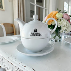White porcelain teapot‑and‑cup set from La Route des Comptoirs with the boat‑and‑tea‑leaf logo on each piece