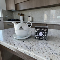 White porcelain teapot‑and‑cup set from La Route des Comptoirs with the boat‑and‑tea‑leaf logo on each piece
