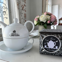 White porcelain teapot‑and‑cup set from La Route des Comptoirs with the boat‑and‑tea‑leaf logo on each piece