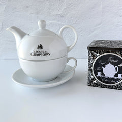 White porcelain teapot‑and‑cup set from La Route des Comptoirs with the boat‑and‑tea‑leaf logo on each piece