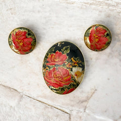 Hand-painted floral brooch and screw-back earrings set in lacquered wood with gold-tone trim, featuring red and pink flowers on a black background, signed by the artist.