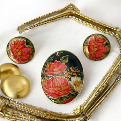 Hand-painted floral brooch and screw-back earrings set in lacquered wood with gold-tone trim, featuring red and pink flowers on a black background, signed by the artist.