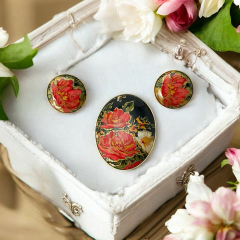 Hand-painted floral brooch and screw-back earrings set in lacquered wood with gold-tone trim, featuring red and pink flowers on a black background, signed by the artist.