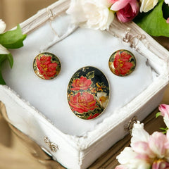 Hand-painted floral brooch and screw-back earrings set in lacquered wood with gold-tone trim, featuring red and pink flowers on a black background, signed by the artist.
