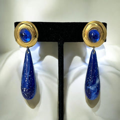 Vintage pierced earrings featuring glossy faux lapis long teardrop pendants and round blue cabochons set in gold-tone metal; likely acrylic components with cosmic speckled finish, measuring approx. 2¼" long, in very good vintage condition with minor glue visible on one cabochon edge.