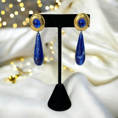 Vintage pierced earrings featuring glossy faux lapis long teardrop pendants and round blue cabochons set in gold-tone metal; likely acrylic components with cosmic speckled finish, measuring approx. 2¼" long, in very good vintage condition with minor glue visible on one cabochon edge.