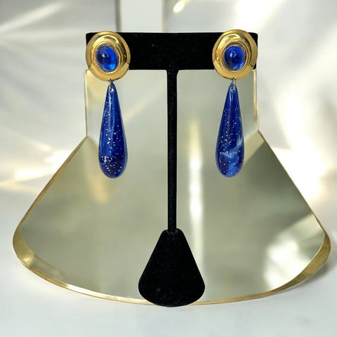 Vintage pierced earrings featuring glossy faux lapis long teardrop pendants and round blue cabochons set in gold-tone metal; likely acrylic components with cosmic speckled finish, measuring approx. 2¼" long, in very good vintage condition with minor glue visible on one cabochon edge.
