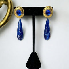 Vintage pierced earrings featuring glossy faux lapis long teardrop pendants and round blue cabochons set in gold-tone metal; likely acrylic components with cosmic speckled finish, measuring approx. 2¼" long, in very good vintage condition with minor glue visible on one cabochon edge.