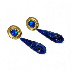 Vintage pierced earrings featuring glossy faux lapis long teardrop pendants and round blue cabochons set in gold-tone metal; likely acrylic components with cosmic speckled finish, measuring approx. 2¼" long, in very good vintage condition with minor glue visible on one cabochon edge.