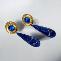 Vintage pierced earrings featuring glossy faux lapis long teardrop pendants and round blue cabochons set in gold-tone metal; likely acrylic components with cosmic speckled finish, measuring approx. 2¼" long, in very good vintage condition with minor glue visible on one cabochon edge.