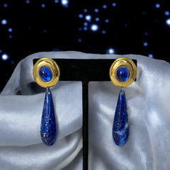 Vintage pierced earrings featuring glossy faux lapis long teardrop pendants and round blue cabochons set in gold-tone metal; likely acrylic components with cosmic speckled finish, measuring approx. 2¼" long, in very good vintage condition with minor glue visible on one cabochon edge.