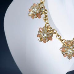 Gold tone statement necklace with five floral pendants featuring peach, champagne, and clear crystals in marquise, square, pear, and chaton cuts; adjustable curb chain with lobster clasp.