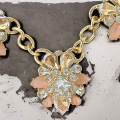 Gold tone statement necklace with five floral pendants featuring peach, champagne, and clear crystals in marquise, square, pear, and chaton cuts; adjustable curb chain with lobster clasp.