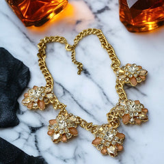 Gold tone statement necklace with five floral pendants featuring peach, champagne, and clear crystals in marquise, square, pear, and chaton cuts; adjustable curb chain with lobster clasp.