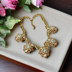 Gold tone statement necklace with five floral pendants featuring peach, champagne, and clear crystals in marquise, square, pear, and chaton cuts; adjustable curb chain with lobster clasp.