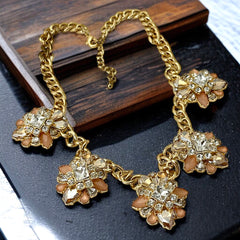 Gold tone statement necklace with five floral pendants featuring peach, champagne, and clear crystals in marquise, square, pear, and chaton cuts; adjustable curb chain with lobster clasp.