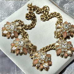 Gold tone statement necklace with five floral pendants featuring peach, champagne, and clear crystals in marquise, square, pear, and chaton cuts; adjustable curb chain with lobster clasp.