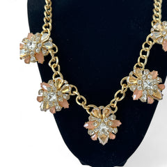 Gold tone statement necklace with five floral pendants featuring peach, champagne, and clear crystals in marquise, square, pear, and chaton cuts; adjustable curb chain with lobster clasp.