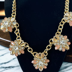 Gold tone statement necklace with five floral pendants featuring peach, champagne, and clear crystals in marquise, square, pear, and chaton cuts; adjustable curb chain with lobster clasp.
